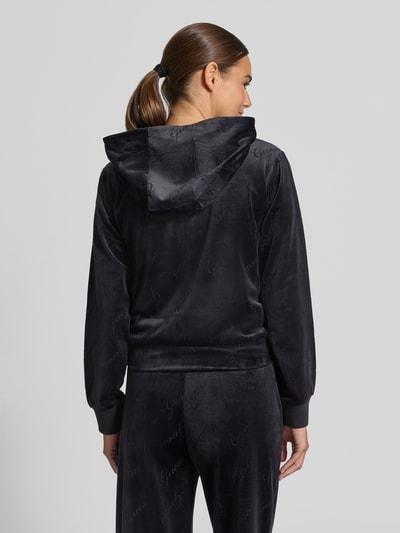 Frauenmodel trägt GUESS Sweatjacke mit Logo-Muster Modell 'LOREN', Schwarz, weiche Textur, Kapuze, Rückenansicht, Ganzkörperansicht Rückansicht.