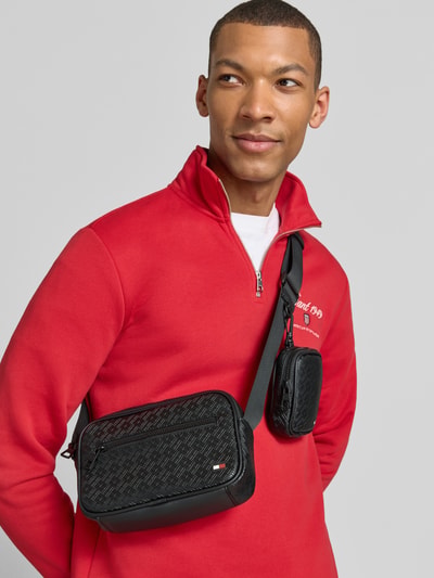Männermodel trägt Umhängetasche mit Label-Detail Modell 'EMBOSSED FLAG MODULAR' von Tommy Hilfiger in Lederoptik, Schwarz, Hauptfach, Reißverschlussfach, Netzfach, Reißverschlusstasche, Flag-Monogram Muster, Logo-Detail, Schulterriemen, Kunstleder, Ganzkörperansicht von vorne.
