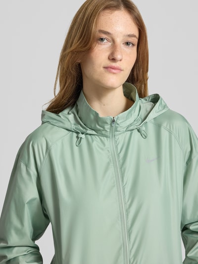 Frauenmodel trägt Regular Fit Jacke mit Stehkragen Modell 'Tempo' von NIKE TRAINING in Mintgrün, glatte Textur, Kapuze mit Tunnelzug, Reißverschluss und Eingrifftaschen, elastische Abschlüsse, Nahaufnahme Oberkörper. Rückenlänge 60 cm, Schulterbreite 54 cm, Brustweite 50 cm, Ärmellänge 59 cm bei Größe S.