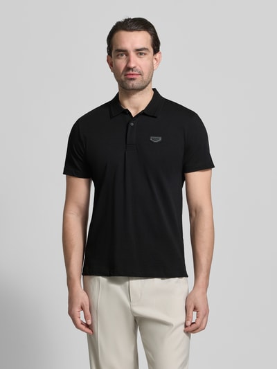 Männermodel trägt Slim Fit Polo-Shirt mit Logo-Applikation von Antony Morato in Schwarz, reine Baumwolle, Polokragen, Ganzkörperansicht von vorne.