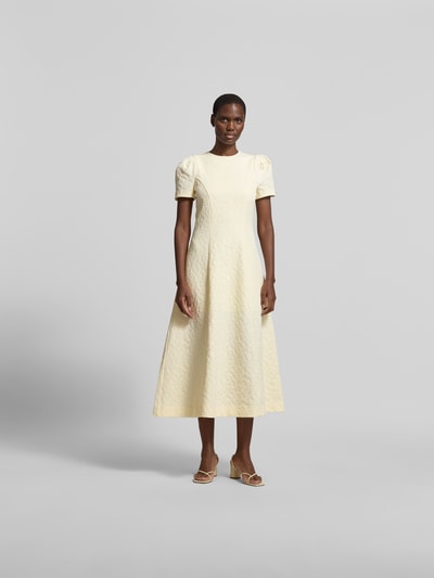 Frauenmodel trägt Midikleid mit floralem Allover-Detail von ROTATE, gelb, Elastischer-Material-Mix, A-Linie, Kurzärmelig, taillierte Passform, Ganzkörperansicht von vorne.