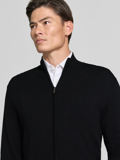Männermodel trägt Slim Fit Strickjacke aus Viskose-Mix mit Stehkragen von MCNEAL in Schwarz, Reißverschluss, Nahaufnahme Oberkörper.