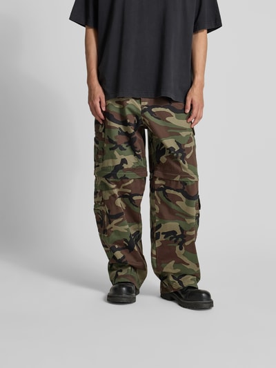 Männermodel trägt Relaxed Fit Cargohose aus Baumwolle von VETEMENTS mit Camouflage-Muster, Cargotaschen, Eingriffstaschen, Ganzkörperansicht von vorne. Reine Baumwolle, Knopf-Reißverschluss, Gürtelschlaufen, Innenbeinlänge 81 cm, Bundweite 45 cm bei Größe 32.