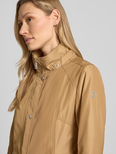 Vrouwenmodel draagt Regular Fit Jacke mit Logo-Print van Fuchs Schmitt in lichtbruin, glad oppervlak, staande kraag, capuchon met tunnelkoord, ritszakken, schouderbreedte 40 cm, borstwijdte 51 cm, ruglengte 71 cm, mouwlengte 66 cm, detailopname bovenlichaam.