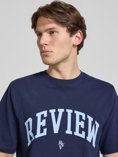 Männermodel trägt T-shirt mit labelprint en ronde hals van REVIEW in donkerblauw, puur katoen, regular fit, nahaufnahme bovenlichaam.