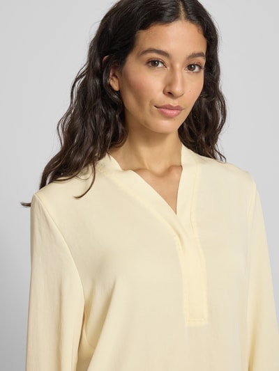 Vrouwenmodel draagt Regular Fit Bluse mit V-Ausschnitt van Marc Cain in lichtgeel, gladde stof, label-detail, Nahaufnahme bovenlichaam.