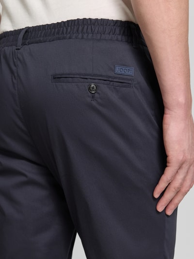 Männermodel trägt Regular Fit Stoffhose mit Logo-Detail Modell 'Lester' von JOOP! Collection im Baumwoll-Mix mit Bundfalten, Detailaufnahme Rückansicht.