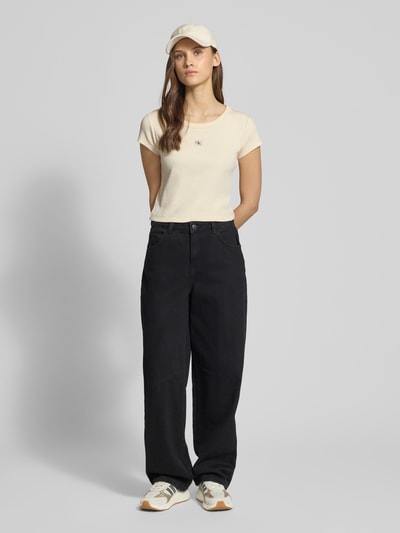 Modelka nosi Cropped T-Shirt in Ripp-Optik mit Label-Badge od Calvin Klein Jeans, bawełna z elastanem, kremowy, długość tyłu w rozmiarze S: 36 cm, widok całej sylwetki z przodu.