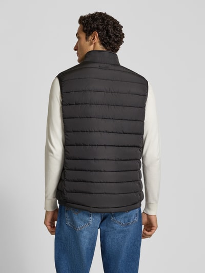 Männermodel trägt Steppweste mit Stehkragen und Eingrifftaschen von Christian Berg Men in Schwarz, gerade Linien, glatte Struktur, Ganzkörperansicht Rückansicht. Rückenlänge 70 cm, Schulterbreite 44 cm, Brustweite 58 cm, Regular Fit, Reißverschluss.