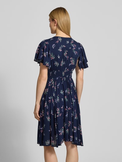 Frauenmodel trägt Knielanges Kleid aus Viskose mit V-Ausschnitt von Apricot in Dunkelblau mit Allover-Look, A-Linie, Knopfleiste, Elastisches Taillenband, Knielänge, Rückenlänge 104 cm, Brustweite 44 cm, Ärmellänge 21 cm, Ganzkörperansicht Rückansicht.