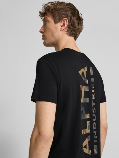 Männermodel trägt T-Shirt aus Baumwolle von Alpha Industries, Gerader-Schnitt, Rundhalsausschnitt, Label-Details, Rückenlänge 67 cm, Ganzkörperansicht Rückansicht.