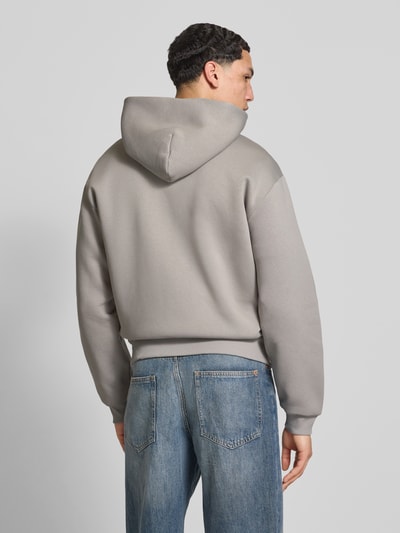 Męski model nosi Sweatjacke mit Känguru-Tasche od REVIEW, bawełniany miks, krój relaxed fit, szary kolor, tylna całkowita długość 68 cm w rozm. M, długość rękawa 62 cm w rozm. M, całkowity widok z tyłu.