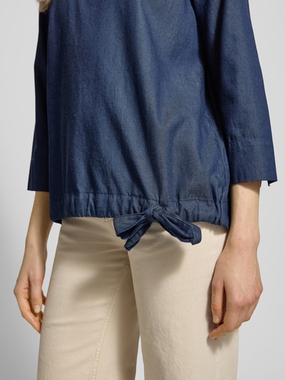 Kobiece modelka nosi Blusenshirt im Denim-Look mit 3/4-Arm von Christian Berg Woman, mieszanka lyocellu i bawełny, krój regular fit, imitacja denimu, okrągły dekolt, rękaw o dł. 3/4, długość tyłu w rozmiarze 36: 63 cm, długość rękawa: 48 cm, tekstura gładka, kolor granatowy, detal wiązania na dole, zbliżenie na górną część ciała