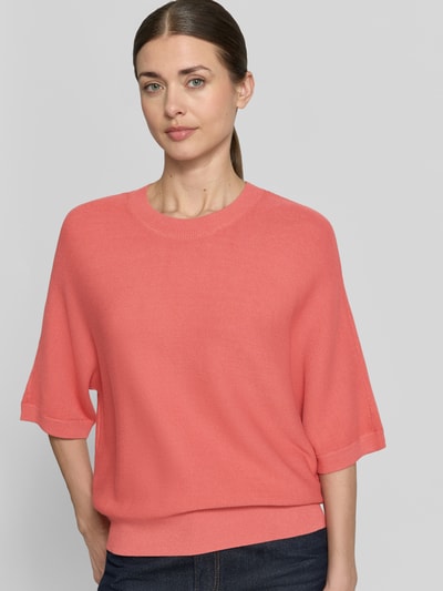 Modelka kobieca nosi Strickpullover aus Viskose-Mix mit Rundhalsausschnitt od MSCH Copenhagen, kolor koralowy, luźny krój, 3/4 rękaw, prążkowany dekolt i wykończenia, długość tyłu 51 cm, długość rękawa 35 cm, widok na górną część ciała z przodu.