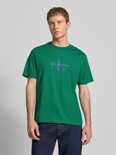 Männermodel trägt T-Shirt mit Label-Print und Rundhalsausschnitt von Calvin Klein Jeans, grün, Reine Baumwolle, Regular-Fit, Ganzkörperansicht von vorne.