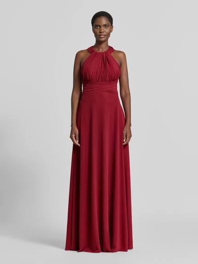 Modelka kobieca nosi 'Abendkleid mit Neckholder und Raffungen' od TROYDEN COLLECTION, czerwony szyfon, fason taliowany, długość maxi, zapięcie na szyi, marszczenia, zamek z tyłu, długość tyłu w rozmiarze 36: 167 cm, szerokość w rozmiarze 36: 28 cm, widok całej sylwetki z przodu.