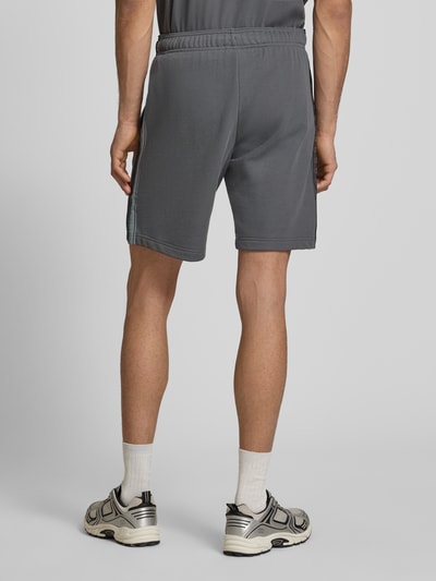 Männermodel trägt graue Shorts mit Logo und elastischem Bund von CHAMPION, Baumwoll-Mix, Regular Fit, Ganzkörperansicht Rückansicht.