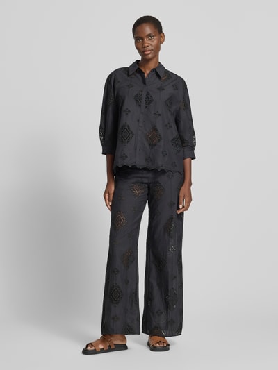 Frauenmodel trägt Hose aus Baumwolle mit Häkelspitze Modell 'MIKE' von Bash in Schwarz, Flared-Cut, Lochmuster, Ganzkörperansicht von vorne.