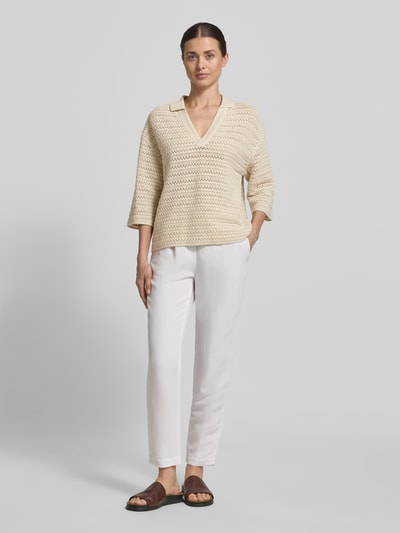 Kobiece model prezentuje sweter z dzianiny z bawełny o kroju relaxed fit, kołnierzyk polo, dekolt w serek, rękaw o dł. 3/4, model 'Garakino' od OPUS, długość tyłu 56 cm, długość rękawów 33 cm, jasne kolory, widoczna faktura dzianiny, gładkie białe spodnie, widok całej sylwetki z przodu.