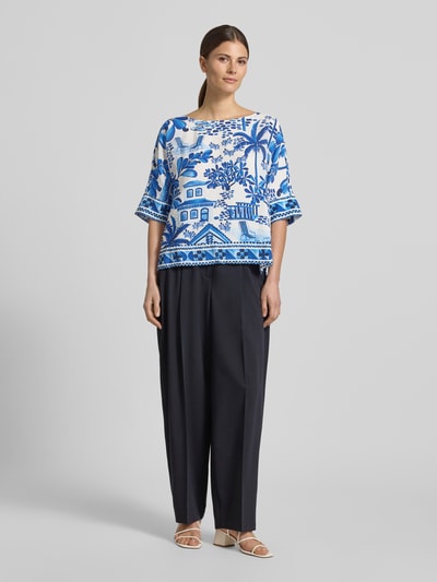 Kobieta nosi Regular Fit Bluse aus Viskose-Mix von Christian Berg Woman, motyw na całej powierzchni, listwa guzikowa, rękaw o dł. 1/2, okrągły dekolt, długość tyłu w rozmiarze 36: 55 cm, długość rękawa w rozmiarze 36: 30 cm, mieszanka odcieni niebieskiego i bieli, obszerne kształty, gładkie tekstury, Ganzkörperansicht von vorne.