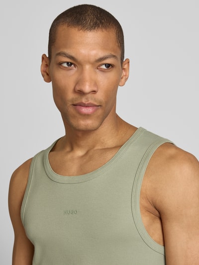 Mannenmodel draagt Slim Fit Tank Top uit katoenmix model 'DAPOTA' van HUGO in effen lichtgroen met labelapplicatie, fijne ribstructuur, close-up bovenlichaam.