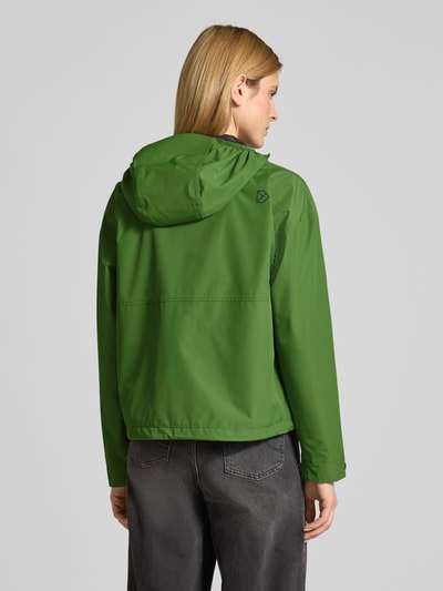 Vrouwenmodel draagt Jacke met Pattentaschen Modell 'MILENA' van Didriksons in recht pasvorm met capuchon, mouwsluitingen, labelprint, geheel ritssluiting, tunnelkoord in band, klepzakken; kleur groen, gladde textuur, ruglengte maat 36: 60 cm, schouderbreedte 60 cm, borstwijdte 55 cm, mouwlengte 66 cm; geheellichaamsaanzicht achteraan.