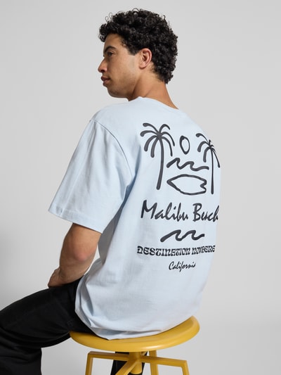 Männermodel trägt Relaxed Fit T-Shirt aus reiner Baumwolle Modell 'MILO' von Only & Sons in Hellblau mit Palmen-Print, Rückansicht