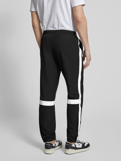 Männermodel trägt Regular Fit Trainingsanzug mit Kontraststreifen von Lacoste Sport in Schwarz mit weißen Streifen, Ganzkörperansicht Rückansicht.