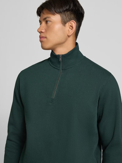 Männermodel trägt Regular Fit Sweatshirt mit Baumwoll-Anteil Modell 'Bradley' von JACK & JONES in Dunkelgrün, Nahaufnahme Oberkörper, Material-Mix, Troyer-Kragen, KI-modifiziertes Bild
