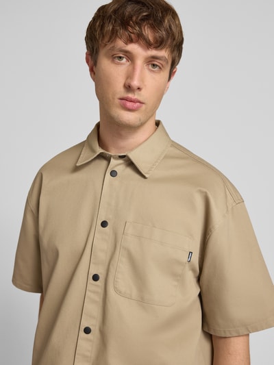 Männermodel trägt Relaxed Fit Freizeithemd mit Brusttasche von REVIEW in Beige, Material-Mix mit Baumwoll-Anteil, Nahaufnahme Oberkörper.