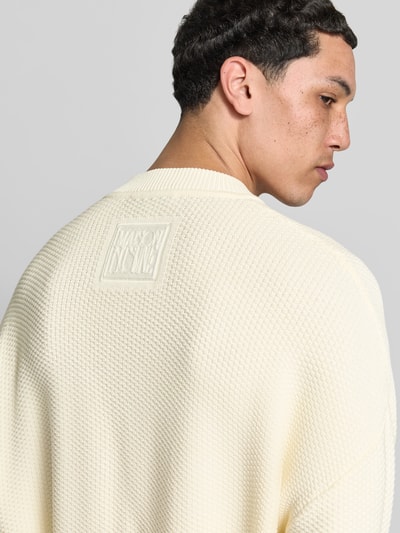 Männermodel trägt Strickjacke mit floralem Stitching von MAISON KITSUNÉ aus Baumwoll-Mix in Creme mit Struktur, Nahaufnahme Rückansicht. Rückenlänge Größe M: 70 cm, Schulterbreite: 45 cm, Ärmellänge: 70 cm, Regular-Fit, elastische Abschlüsse.