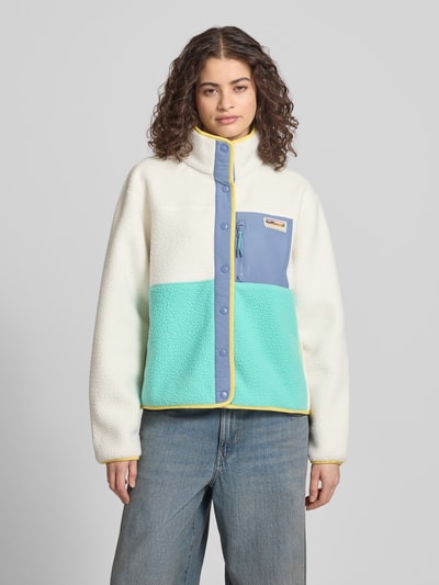 Frauenmodel trägt Fleecejacke mit Brusttasche und Label-Patch von Superdry in Weiß, Hellblau und Mint, Gerader-Schnitt, Stehkragen, Druckknopfverschluss, Rückenlänge 57 cm, Schulterbreite 49 cm, Brustweite 61 cm, Ärmellänge 62 cm, Nahaufnahme Oberkörper.