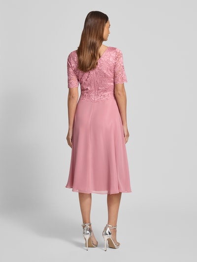 Modelka nosi Knielanges Cocktailkleid mit Spitze und Rundhalsausschnitt von Vera Mont, Szyfon, Linia A, długość do kolan, koronka, okrągły dekolt, długość tyłu w rozmiarze 36: 105 cm, szerokość w rozmiarze 36: 40 cm, długość rękawów w rozmiarze 36: 28 cm, różowy, gładka faktura, całkowity widok z tyłu.
