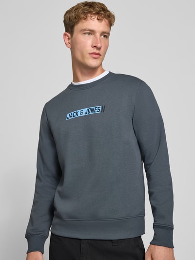Männermodel trägt Regular Fit Sweatshirt mit Baumwoll-Anteil Modell 'Munk' von JACK & JONES, grauer Stoff, Logo-Print, Nahaufnahme Oberkörper, Material-Mix, elastische Abschlüsse, Rundhalsausschnitt.