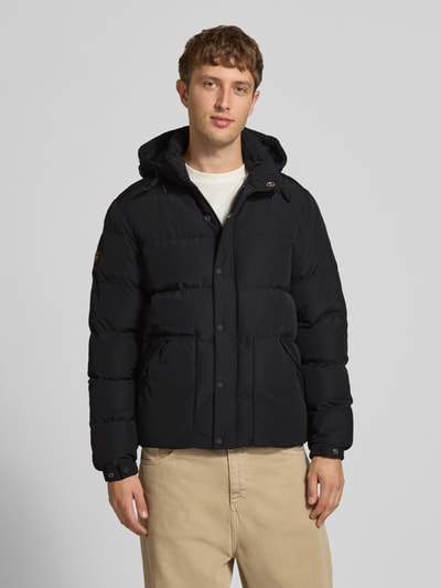 Männermodel trägt zwarte Heren jack met capuchon en trekkoord, recht model, Model 'CLASSIC EVEREST' van Superdry, labelpatch, zijsteekzakken, mouwsluitingen met drukknoop, drukknoopsluiting en ritssluiting, ruglengte maat M 75 cm, schouderbreedte 47 cm, borstwijdte 58 cm, mouwlengte 71 cm, Ganzkörperansicht van voren.