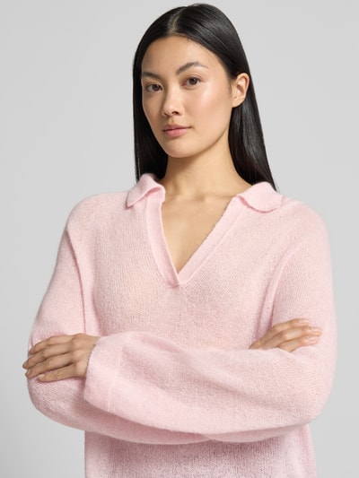 Modelka nosi sweter 'Relaxed Fit Pullover aus Mohair-Alpaka-Mix' od Marc Cain, mieszanka moheru i wełny z alpaki, krój relaxed fit, imitacja dzianiny, wykładany kołnierz z dekoltem w serek, z długim rękawem, różowy kolor, gładka tekstura, długość tyłu w rozmiarze 36: 60 cm, długość rękawa w rozmiarze 36: 68 cm, zbliżenie na górną część ciała.