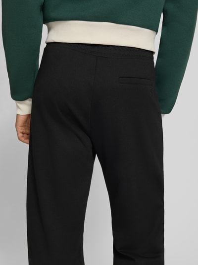Männermodel trägt Straight Fit Sweatpants mit elastischem Bund von REVIEW, Mieszanka materiałów z mieszanką bawełny, krój straight fit, elastyczny pas, kanty, Szerokość w rozmiarze M: 42 cm, Długość wewnętrzna nogawki M: 82 cm, czarny kolor, gładka tekstura, Ganzkörperansicht Rückansicht.