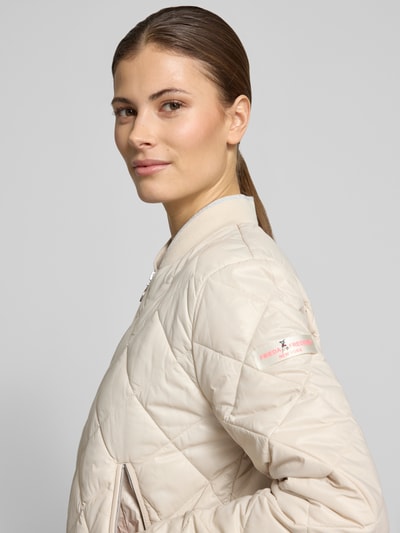 Frauenmodel trägt Steppjacke mit Zweiwege-Reißverschluss Modell 'BOY' von Frieda & Freddies in Beige mit Rautensteppung, Nahaufnahme Oberkörper. Damen Steppjacke, Regular Fit, Stehkragen, Reißverschlusstaschen, Rückenlänge 20 cm, Schulterbreite 16 cm, Brustweite 21 cm, Ärmellänge 24 cm.