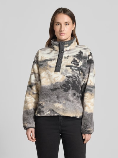 Modelka kobieca nosi Regular Fit Pullover mit Logo-Patch Modell 'Helvetia' od Columbia, kremowo-szare kolory, faktura polaru, napy, kieszeń na piersi, krój regular fit, widok całej sylwetki z przodu.