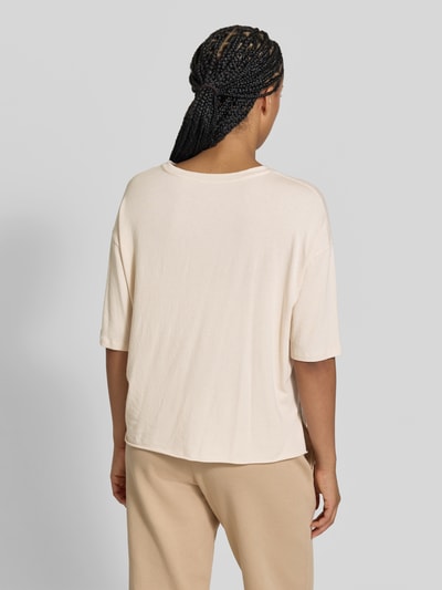 Vrouwenmodel draagt T-shirt met Boothals van Juvia in licht beige, mix van katoen en modal, relaxed fit, halflange mouwen, ruglengte maat S 55 cm, oversneden schouders, effen structuur, Ganzkörperansicht Rückansicht.