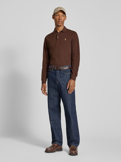 Männermodel trägt Slim Fit Pullover aus Baumwoll-Mix von Polo Ralph Lauren in Braun mit Jeans, Ganzkörperansicht von vorne.