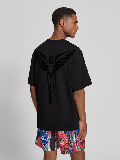 Männermodel trägt Relaxed Fit T-Shirt mit Logo-Stitching Modell 'Ikarus' von COLUCCI, schwarze Baumwolle, Rückansicht, Ganzkörperansicht