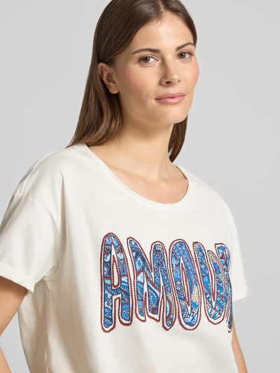 Kobiece model nosi damski t-shirt z obszyciem z kamieni stras T-Shirt mit Strasssteinbesatz od Oui, biała bawełna, prosty krój, dekolt w łódkę, długość tyłu w rozmiarze 36: 60 cm, zbliżenie na górną część ciała.