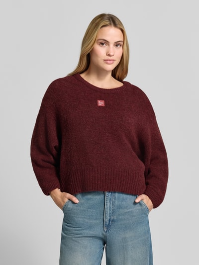 Frauenmodel trägt Oversized Pullover mit Alpaka-Anteil Modell 'East' von American Vintage in dunklem Rot, Strick-Optik, Nahaufnahme Oberkörper.