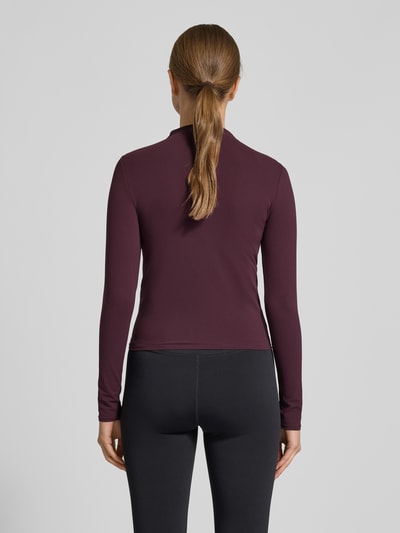 Frauenmodel trägt Slim Fit Longsleeve mit Stehkragen von Fabletics in dunklem Farbton, Elastischer-Material-Mix, Rückenlänge 50 cm, Ganzkörperansicht Rückansicht.