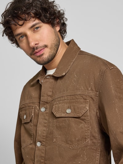 Männermodel trägt Jeansjacke mit Brusttaschen Modell 'Type 10' von Wood Wood, bawełna, krój regular fit, zapięcie na guziki, kolor brązowy, Szerokość w rozmiarze M: 57 cm, długość tyłu w rozmiarze M: 66 cm, długość rękawa w rozmiarze M: 64 cm, Szerokość ramion w rozmiarze M: 55 cm, tekstura spranego denimu, Nahaufnahme Oberkörper.