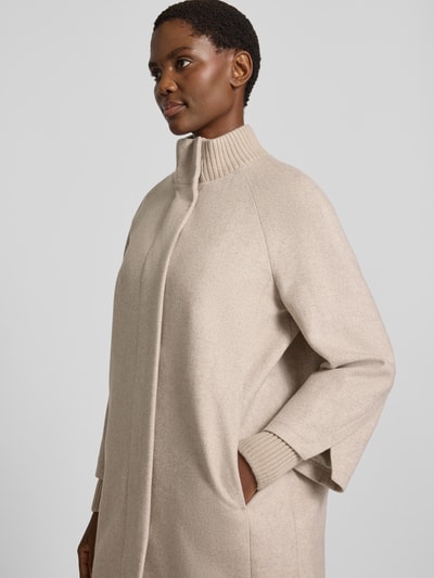 Frauenmodel trägt Mantel aus Woll-Mix mit gestricktem Stehkragen von COMMA in Beige, strukturierte Oberfläche, sichtbarer Druckknopfverschluss, seitliche Eingrifftaschen, gestrickte Ärmelabschlüsse, Nahaufnahme Oberkörper.