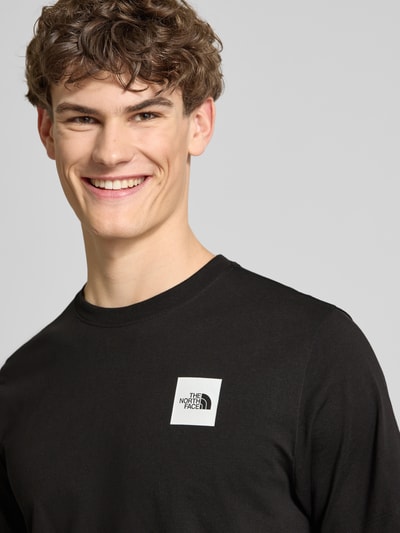 Männermodel trägt T-Shirt aus Baumwoll-Mix Modell 'EVOLUTION' von The North Face in Schwarz mit Label-Print, Nahaufnahme Oberkörper.