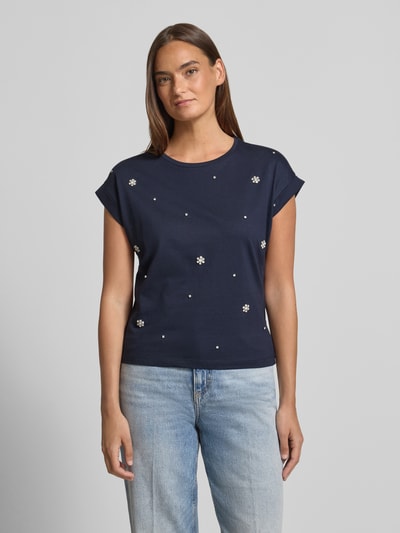 Frauenmodel trägt T-Shirt mit Ziersteinbesatz und Rundhalsausschnitt von Christian Berg Woman aus Reine Baumwolle, Regular-Fit, Rückenlänge bei Größe S 50 cm, navy, mit weißen Ziersteinen auf glatter Oberfläche, Ganzkörperansicht von vorne.