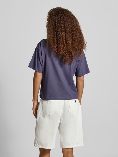 Frauenmodel trägt Regular Fit T-Shirt aus reiner Baumwolle Modell 'CHESTER' von Carhartt Work In Progress in Dunkellila, strukturierte Textur, kombiniert mit weißen Shorts, Kontext: Damen T-Shirt, Stehkragen, Halbarm, Rückenlänge bei Größe S 56 cm, Ganzkörperansicht Rückansicht.